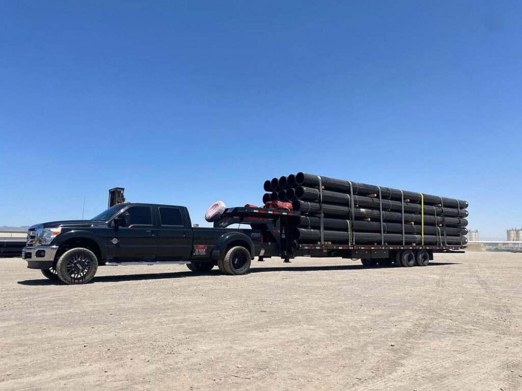 Black dually pickup towing a Maxx-D gooseneck flatbed deckover loaded with steel pipe