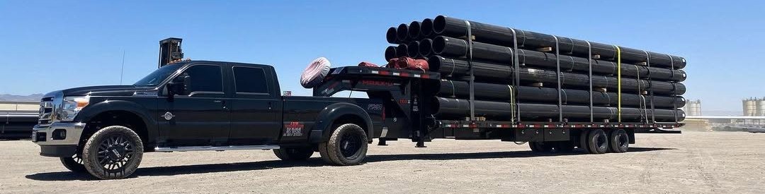 Maxx-D gooseneck deckover flatbed loaded with bundled steel pipe behind a dually pickup