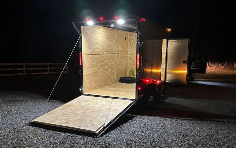 Enclosed cargo trailer at night with the rear ramp door down and interior LED lights on