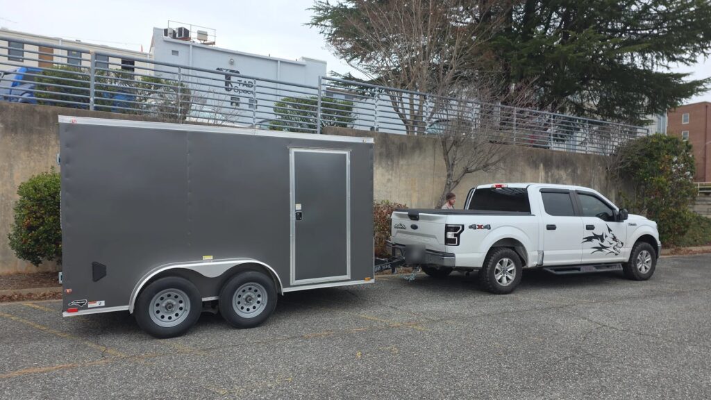Charcoal tandem axle enclosed trailer hooked to a pickup with safety chains crossed, ready to tow