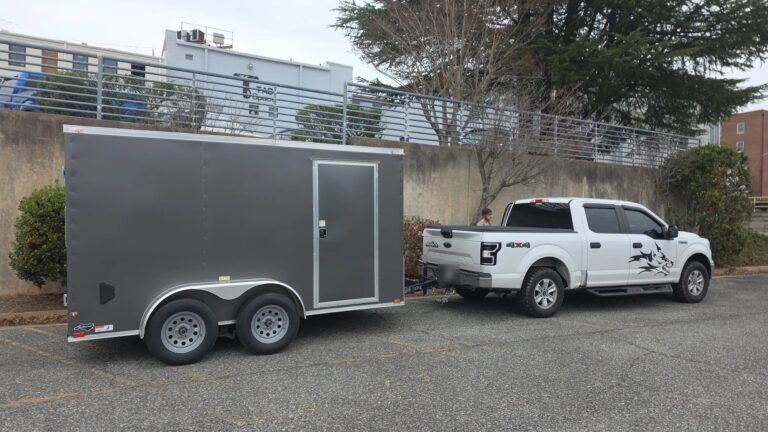 Charcoal tandem axle enclosed trailer hooked to a pickup with safety chains crossed, ready to tow