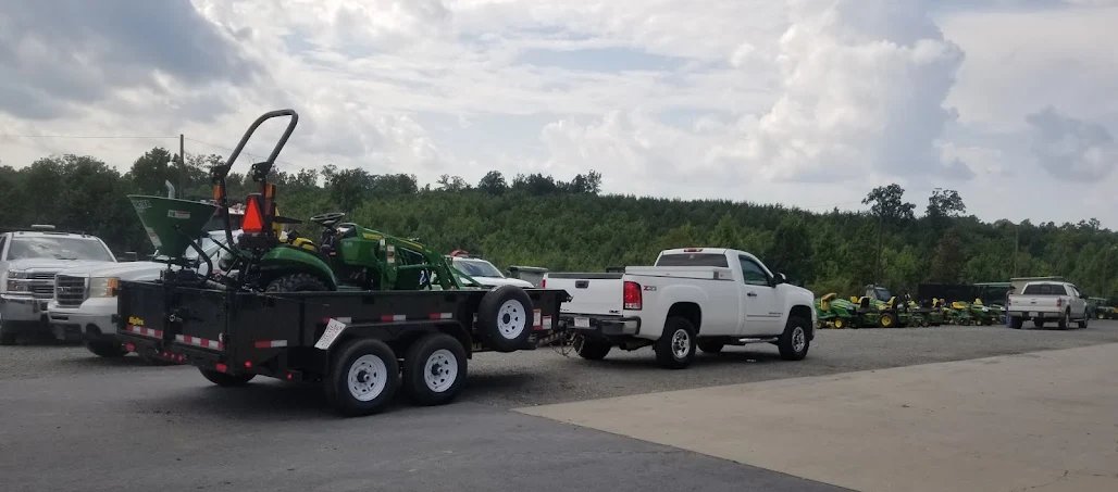 Dump trailer hauling a compact tractor behind a pickup