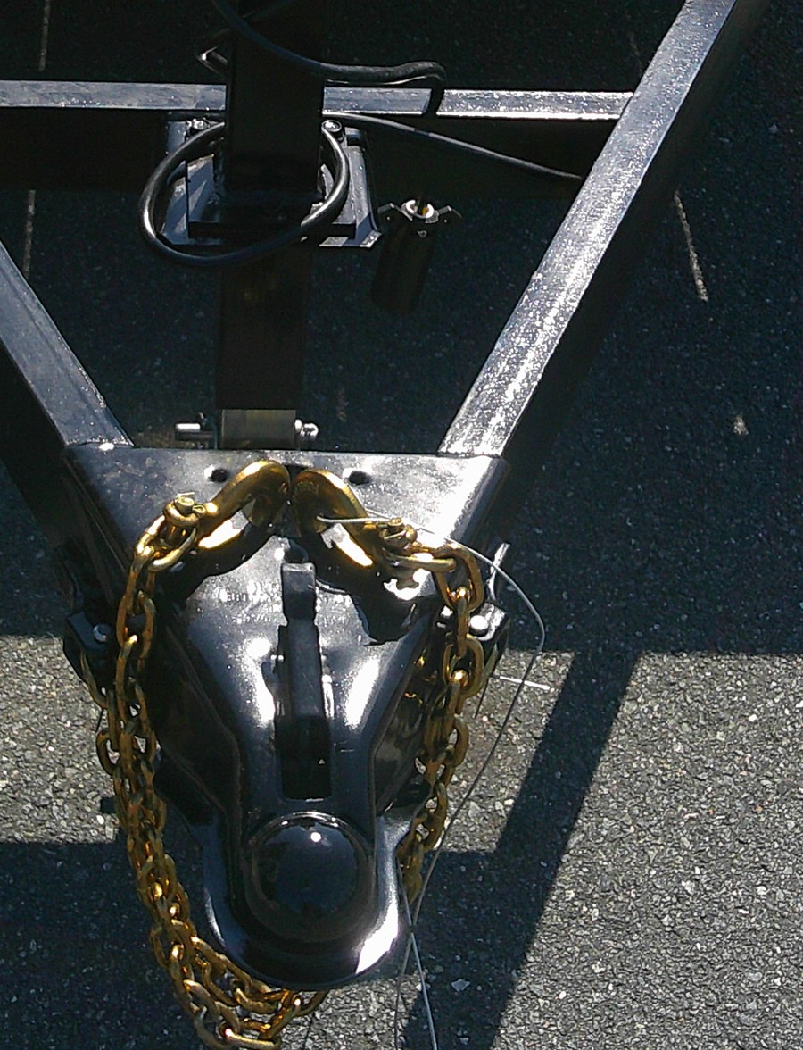 Breakaway switch mounted on a car hauler tongue behind the jack, with its steel pull cable running forward past the coupler and the safety chains